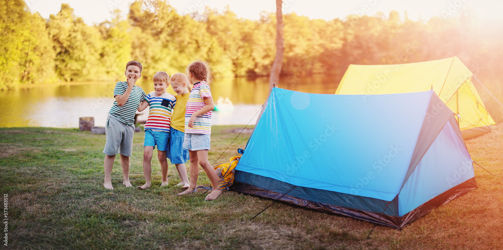 Group of four children standing near colourful tents in nature.