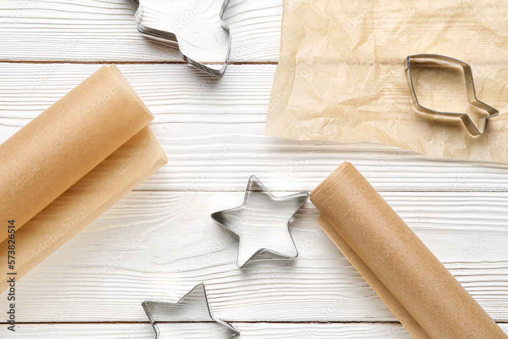 Rolls of baking paper and cookie cutters on light wooden background