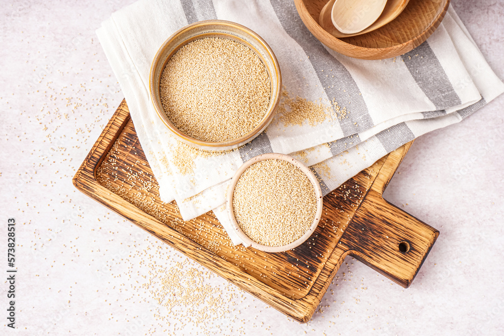 Wooden board with bowls of amaranth seeds on light background