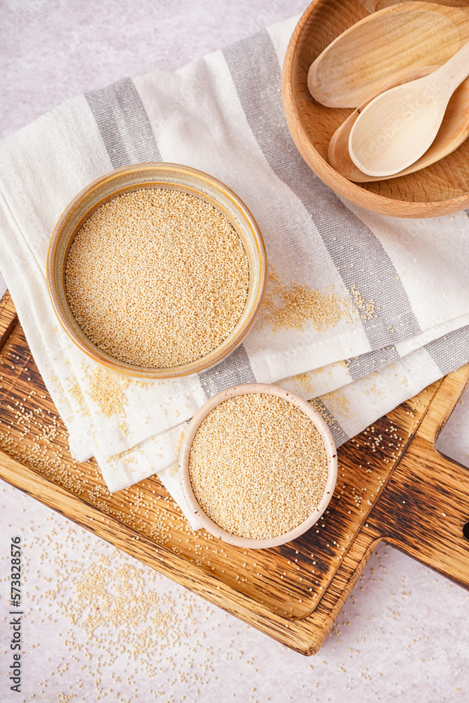 Wooden board with bowls of amaranth seeds on light background, closeup