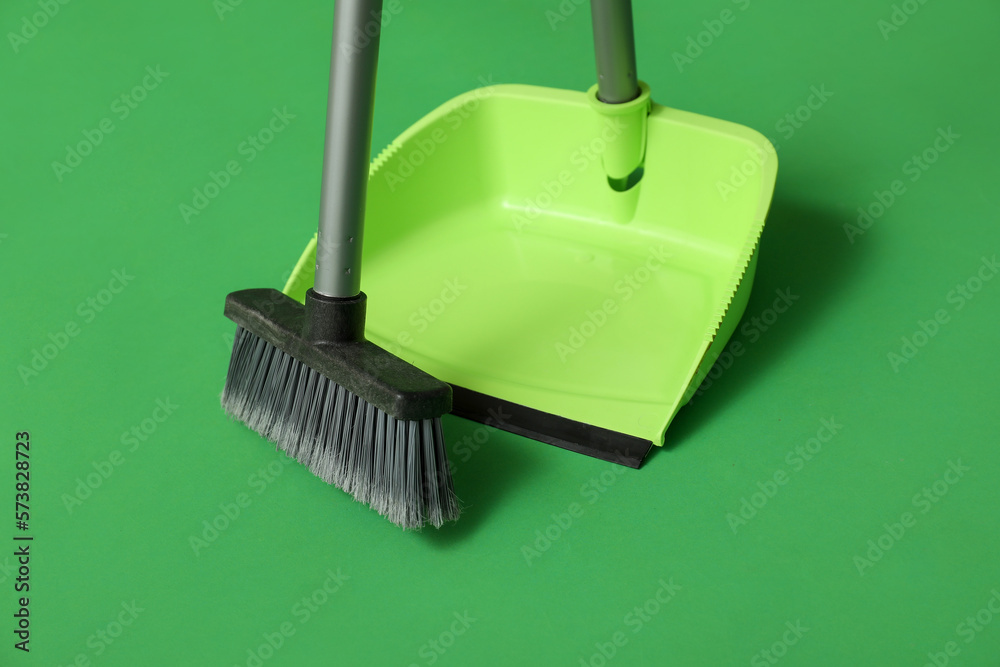 Dustpan with cleaning broom on green background