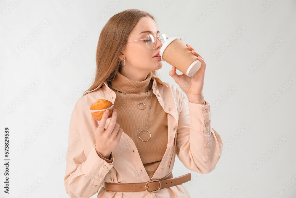 Young woman with tasty cupcake drinking coffee on light background