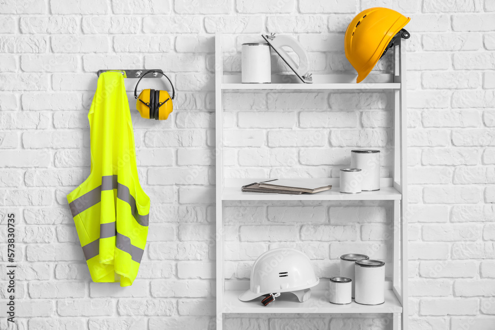 Shelving unit with builders supplies, hearing protectors and reflective vest on white brick wall