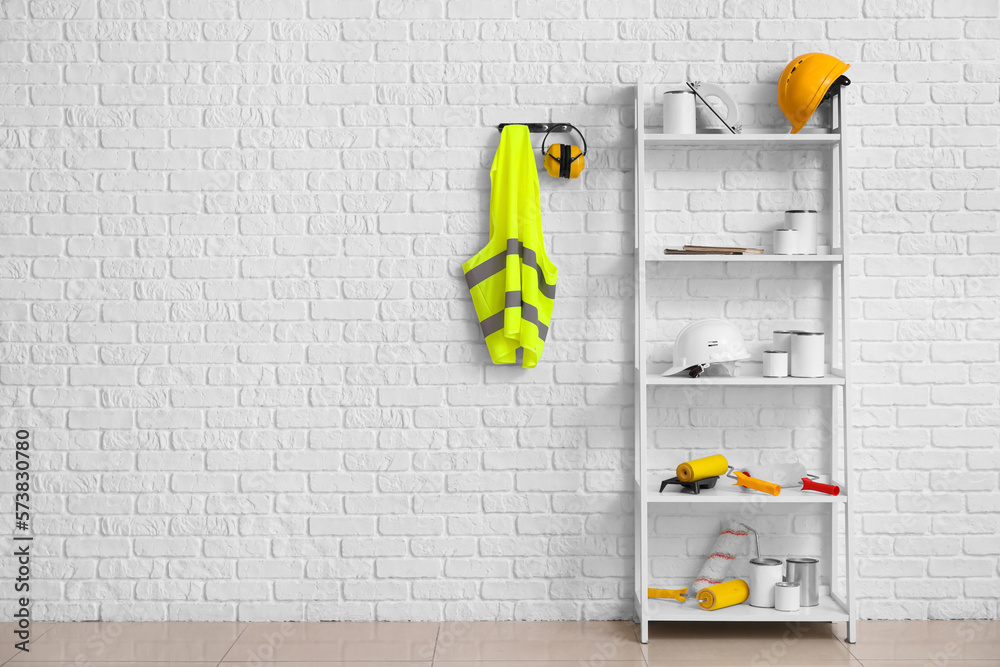 Shelving unit with builders supplies, hearing protectors and reflective vest on white brick wall