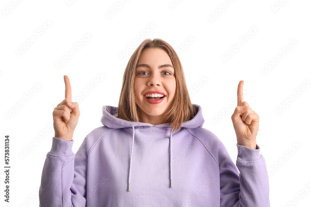 Young woman in lilac hoodie pointing at something on white background