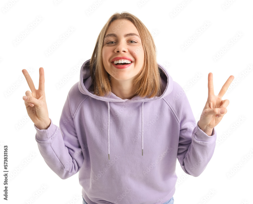 Young woman in lilac hoodie showing victory gesture on white background