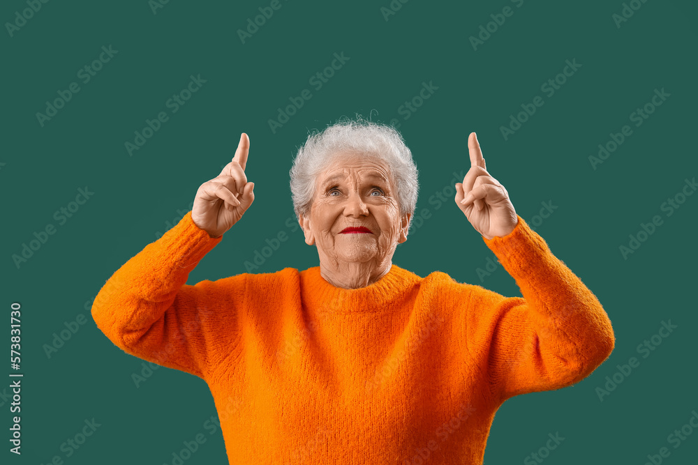 Senior woman in orange sweater pointing at something on green background