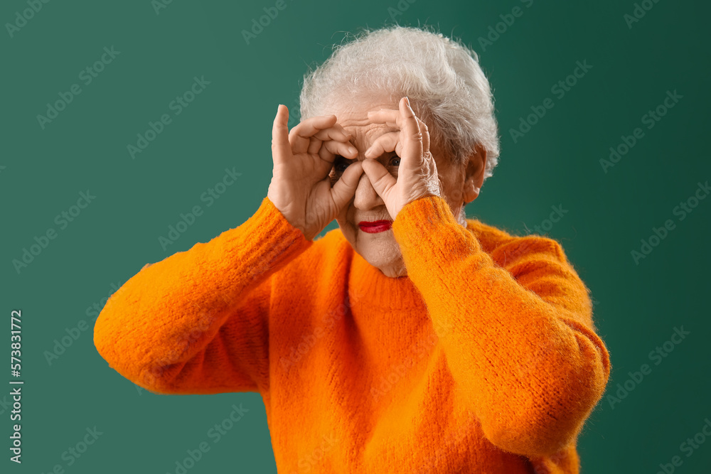 Funny senior woman in orange sweater on green background