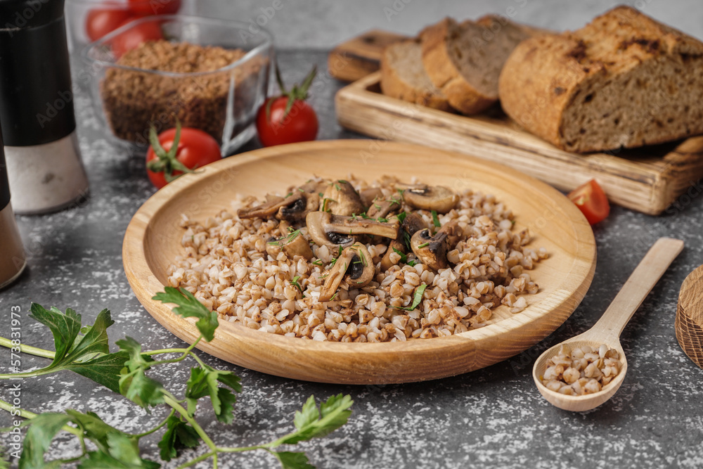 Wooden plate of tasty buckwheat porridge with mushrooms and dill on grey table