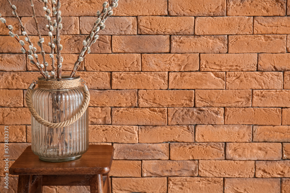 Vase with pussy willow branches on stool near brick wall, closeup