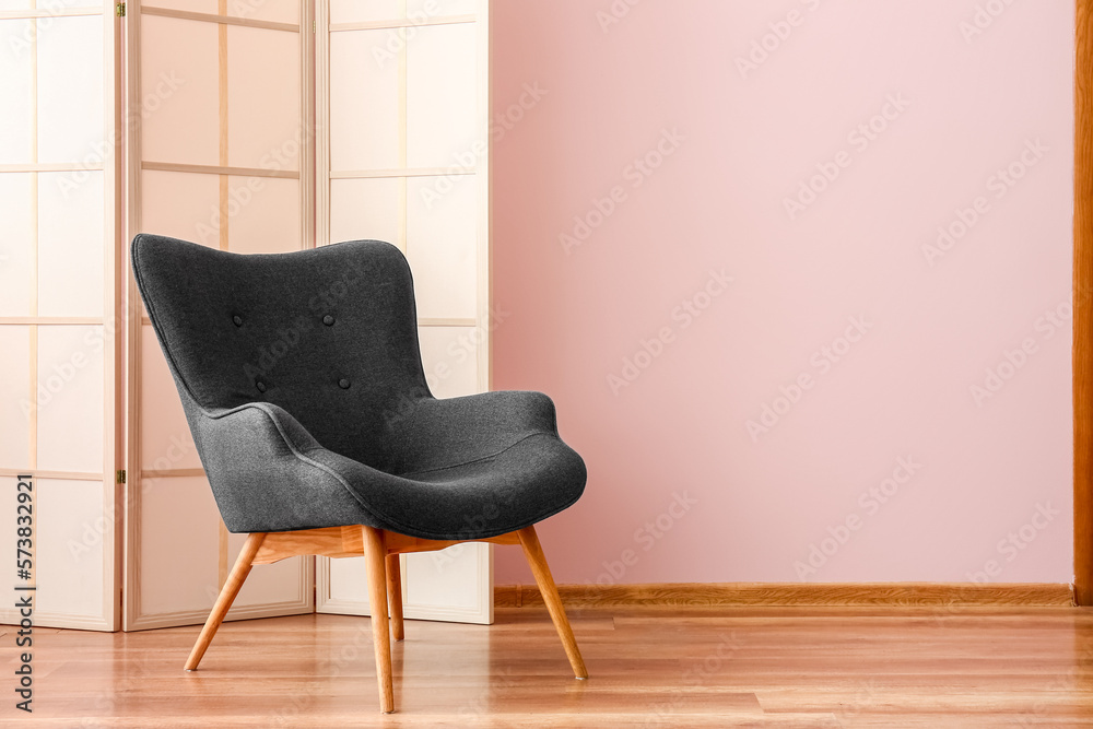 Stylish grey armchair and folding screen near pink wall