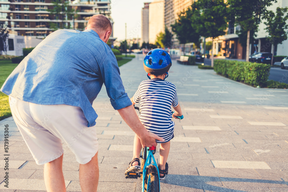 Little boy riding his little bike in a park with his father in the background cheering him. A photo 