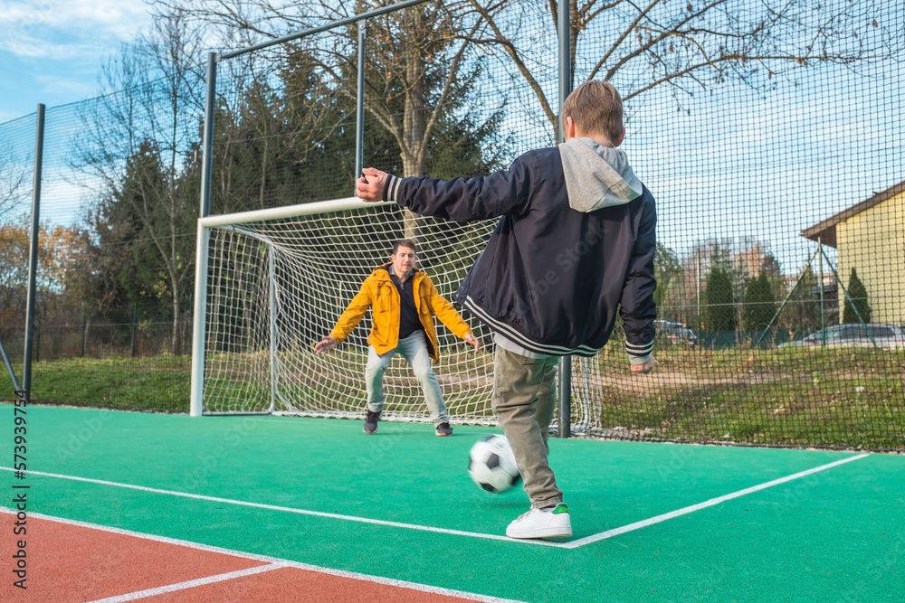 Father and son playing soccer ball on playground, dad teaches soccer