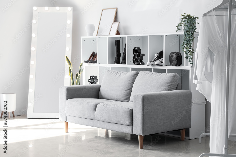 Interior of light dressing room with sofa, shelving unit and mirror