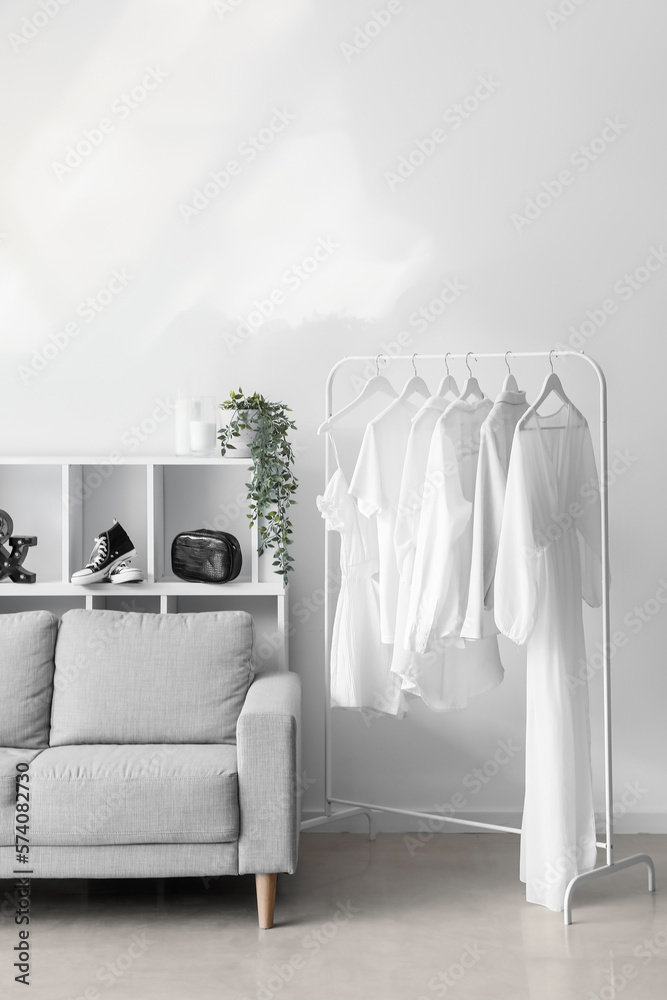 Interior of light dressing room with sofa, shelving unit and clothes