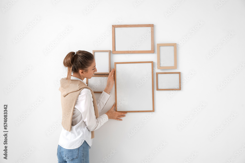 Young woman hanging blank frame on light wall at home