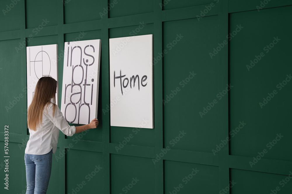 Young woman hanging poster on green wall