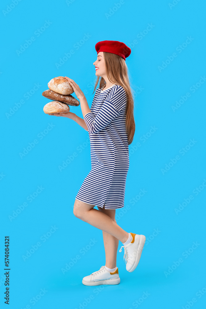 Young woman in beret with loaves of fresh bread on blue background