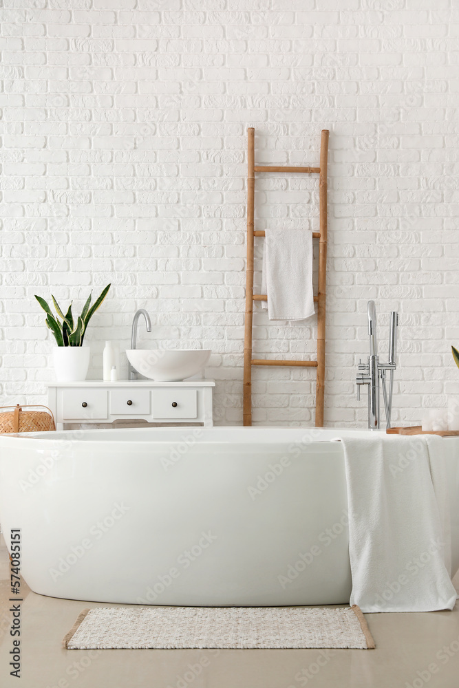 Interior of light bathroom with bathtub, sink and ladder