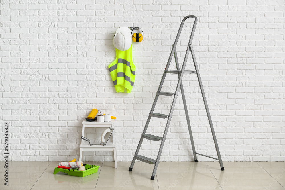 Stepladders with builders supplies near white brick wall