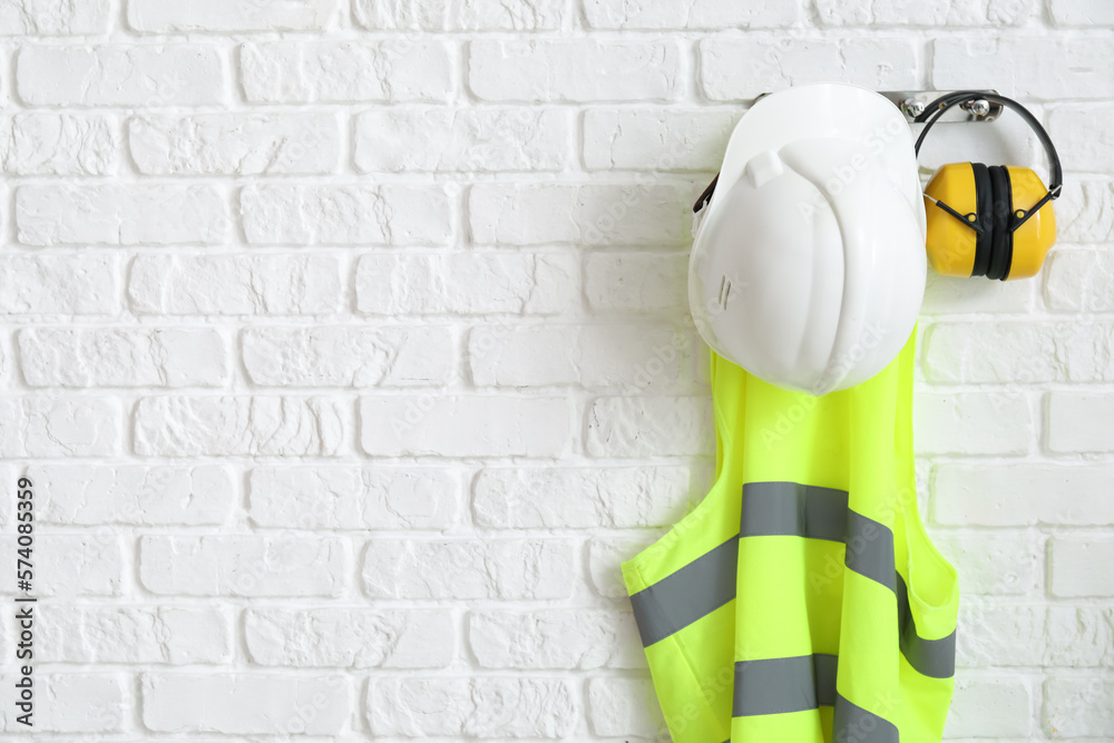 Reflective vest and hearing protectors on white brick wall