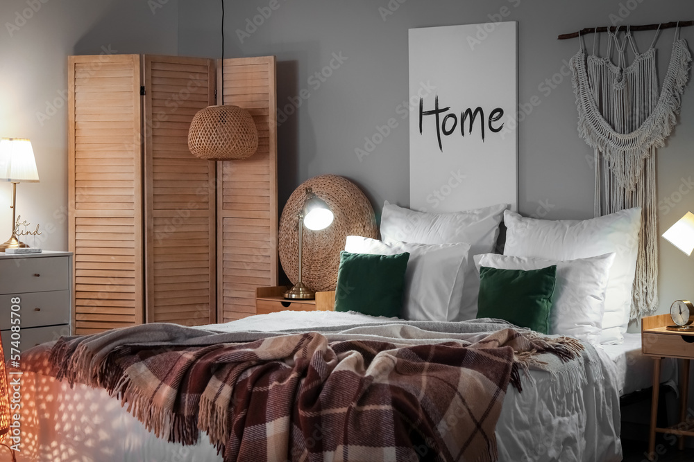 Interior of bedroom with brown checkered blankets on bed and glowing lamps late in evening