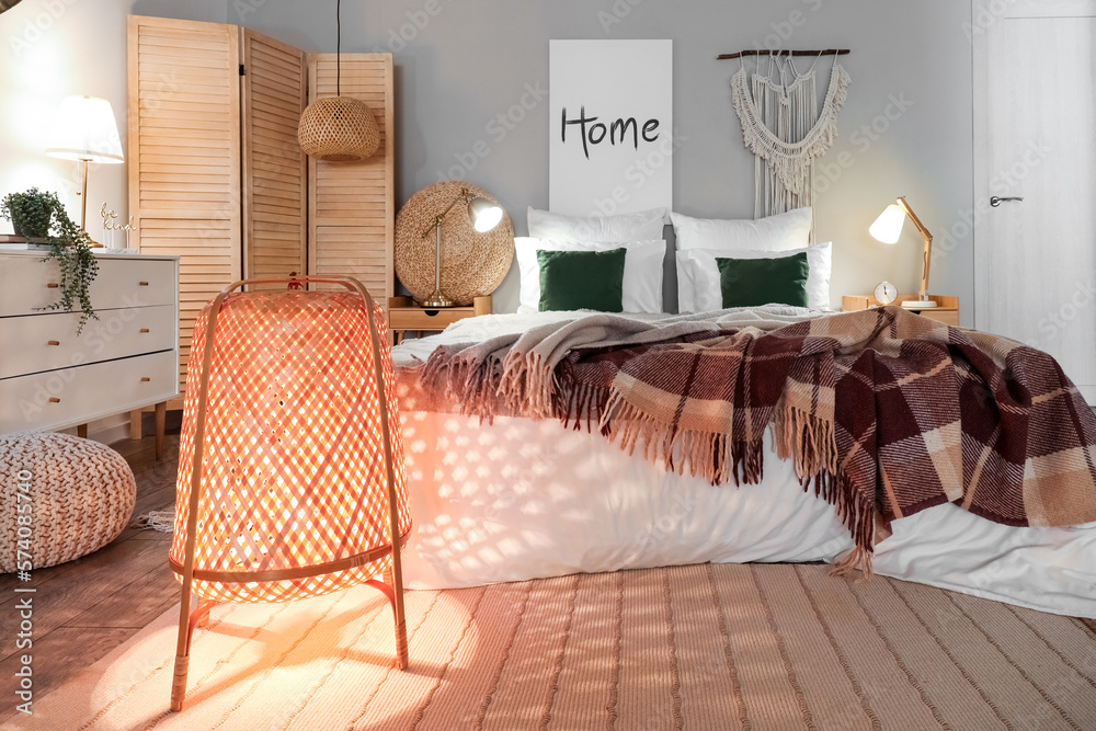 Interior of bedroom with brown checkered blankets on bed and glowing lamps late in evening