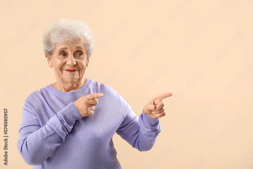 Senior woman in lilac sweater pointing at something on beige background