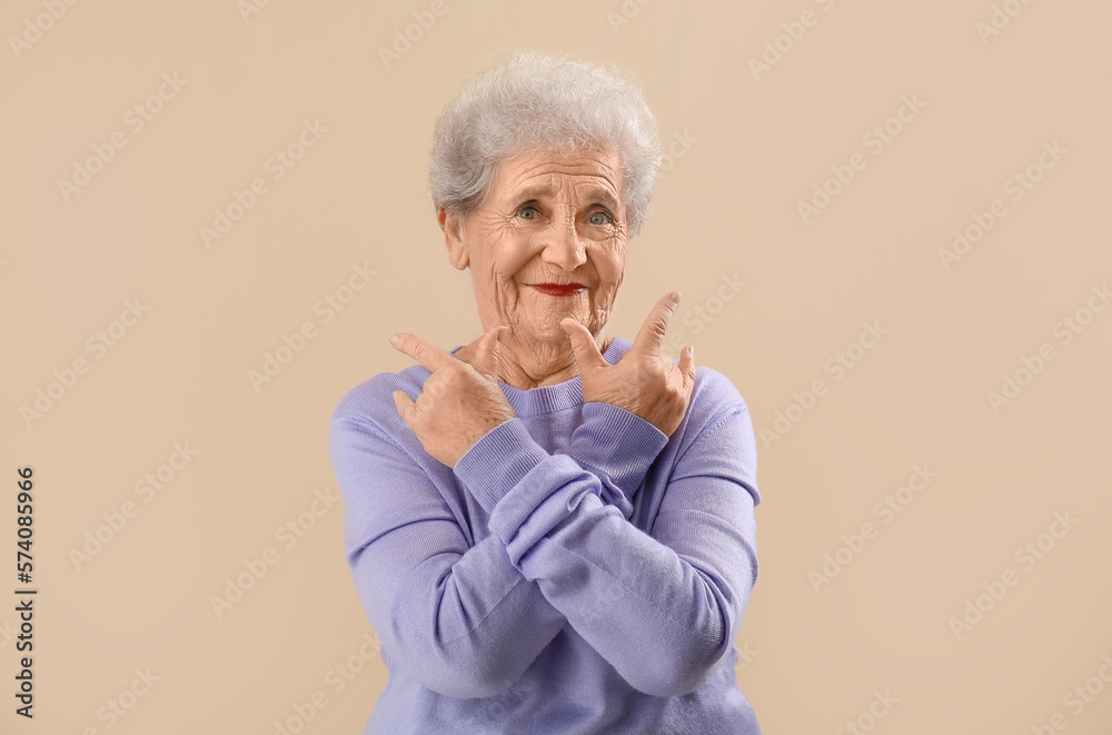 Senior woman in lilac sweater showing  i love you  gesture on beige background