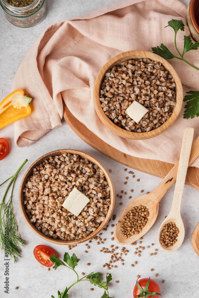 Wooden bowls of tasty buckwheat porridge with butter and vegetables on grey table