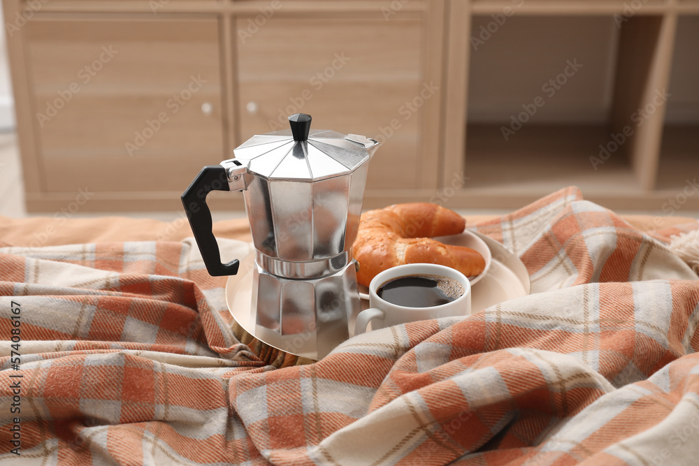 Plate with geyser coffee maker, delicious croissant and cup of espresso on bed