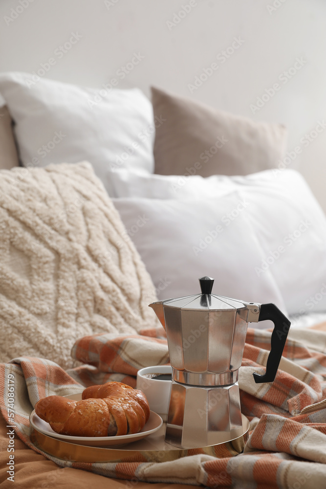 Plate with geyser coffee maker, delicious croissant and cup of espresso on bed