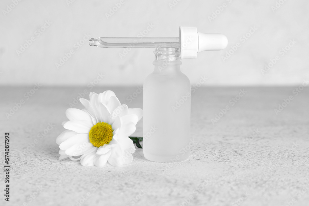 Bottle of essential oil and chamomile flower on light background