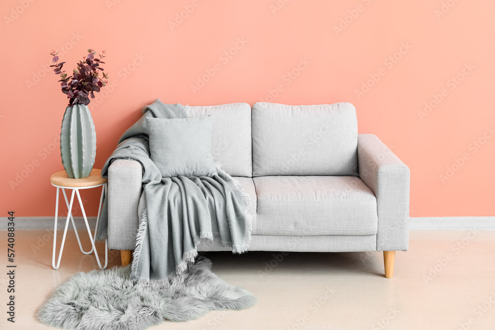 Vase with eucalyptus on table and grey sofa near pink wall