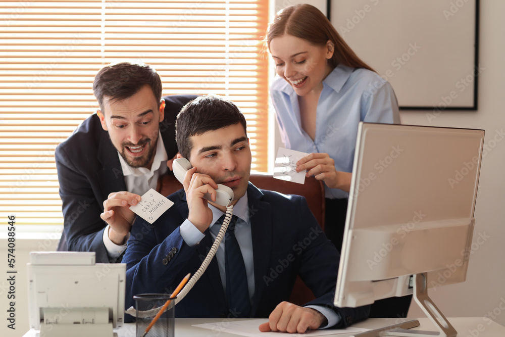 Young man and woman playing a prank on their colleague in office. April Fools Day celebration