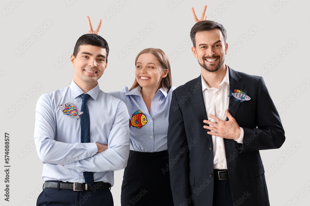 Business colleagues with paper fishes on light background. April Fools Day celebration