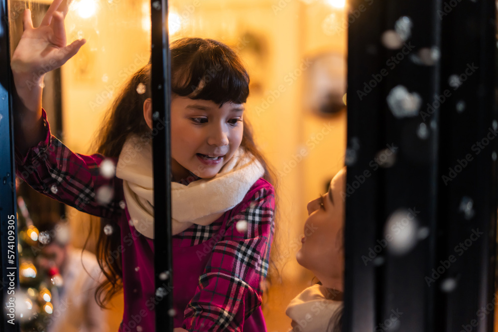 Adorable child looking at the window and admire snowflakes with mother.