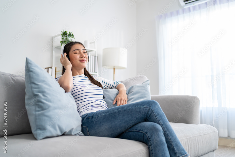 Asian woman listen to music and dancing while sitting on sofa house.