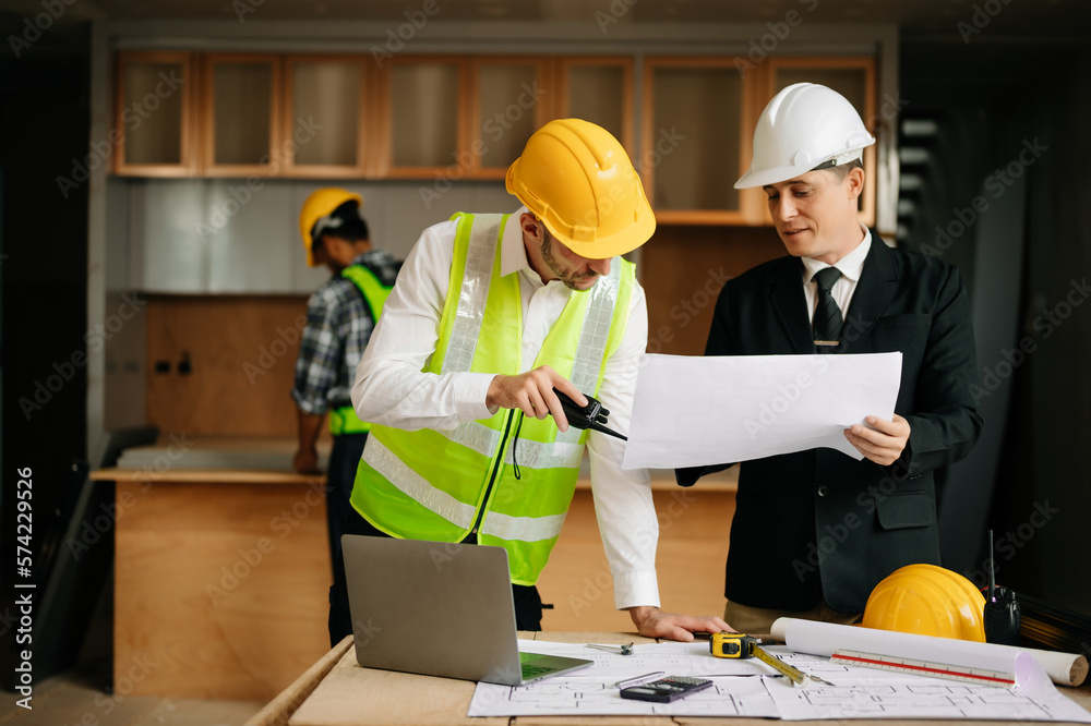 Contractor and architect looking at plan, tablet, laptop and talking about working on big project. B