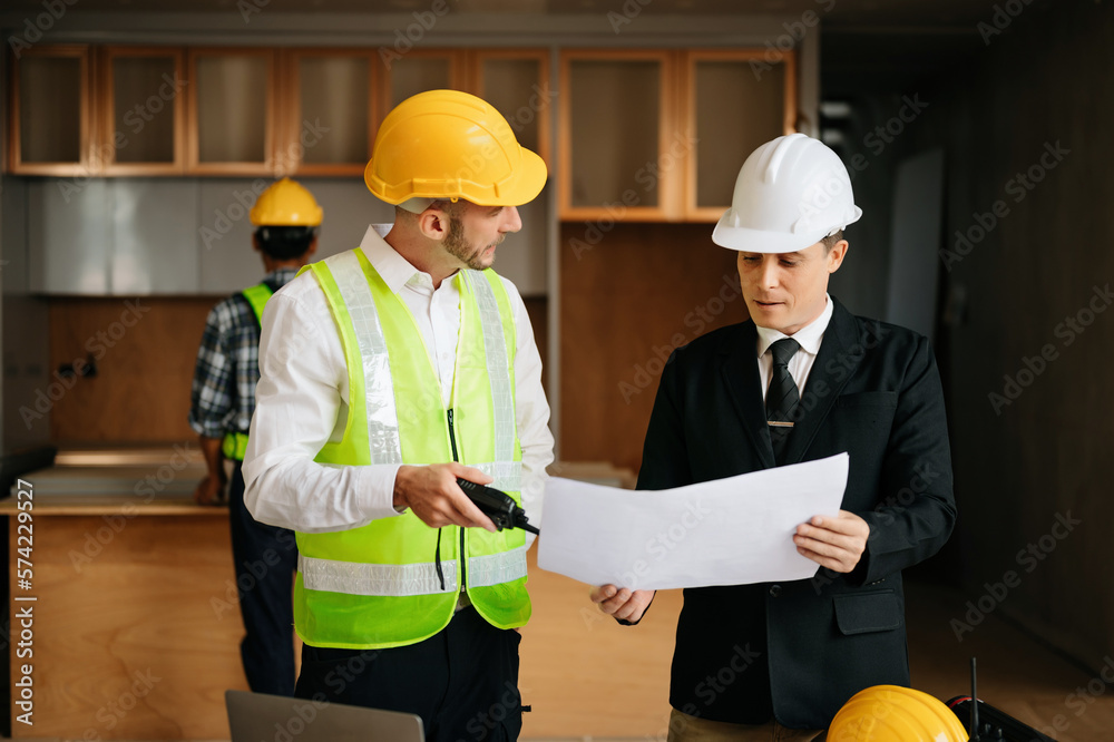 Contractor and architect looking at plan, tablet, laptop and talking about working on big project. B