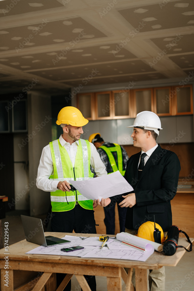 Contractor and architect looking at plan, tablet, laptop and talking about working on big project. B