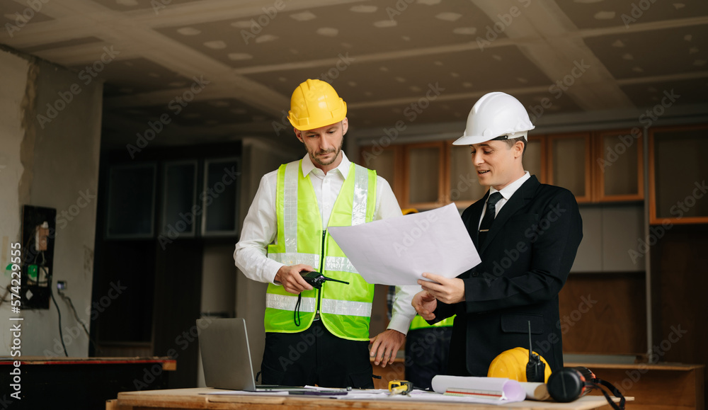 Contractor and architect looking at plan, tablet, laptop and talking about working on big project. B