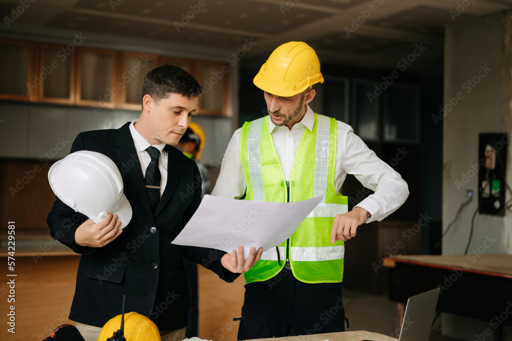 Contractor and architect looking at plan, tablet, laptop and talking about working on big project. B