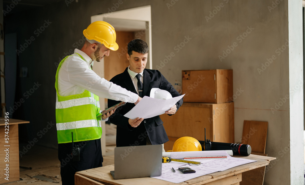 Contractor and architect looking at plan, tablet, laptop and talking about working on big project. B