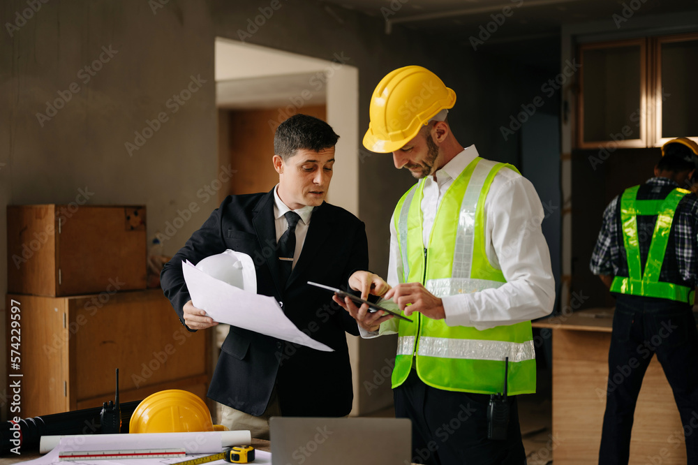 Contractor and architect looking at plan, tablet, laptop and talking about working on big project. B