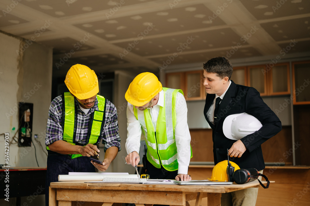 Contractor and architect looking at plan, tablet, laptop and talking about working on big project. B