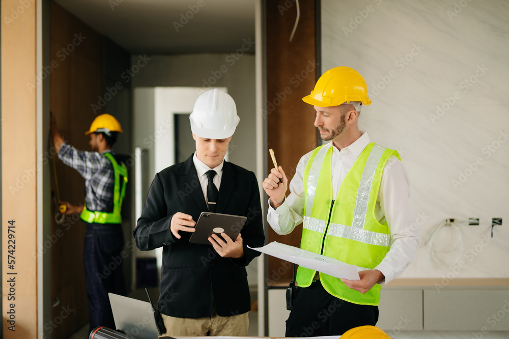 Contractor and architect looking at plan, tablet, laptop and talking about working on big project. B