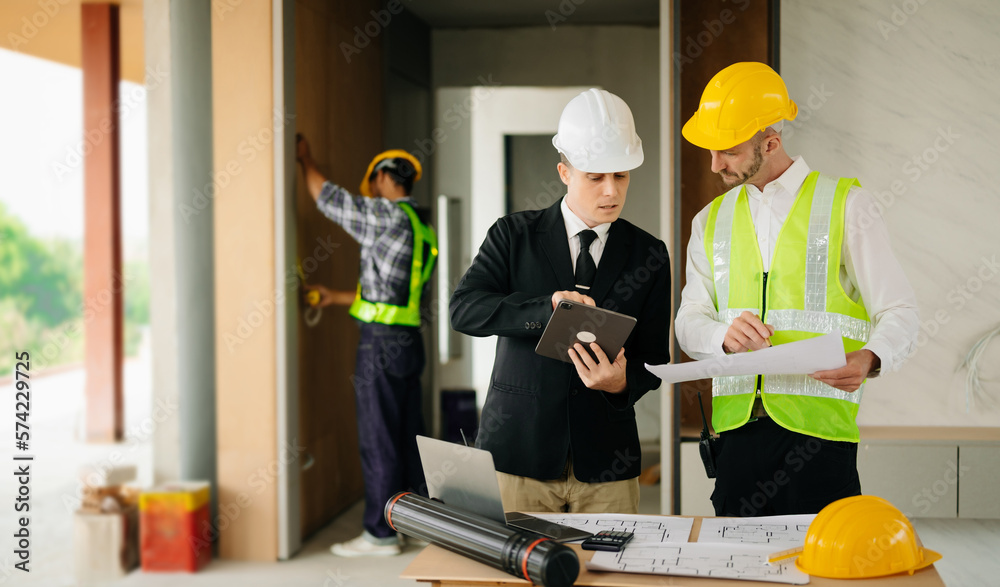 Contractor and architect looking at plan, tablet, laptop and talking about working on big project. B