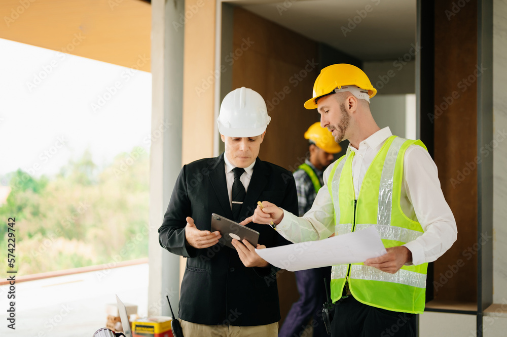 Contractor and architect looking at plan, tablet, laptop and talking about working on big project. B