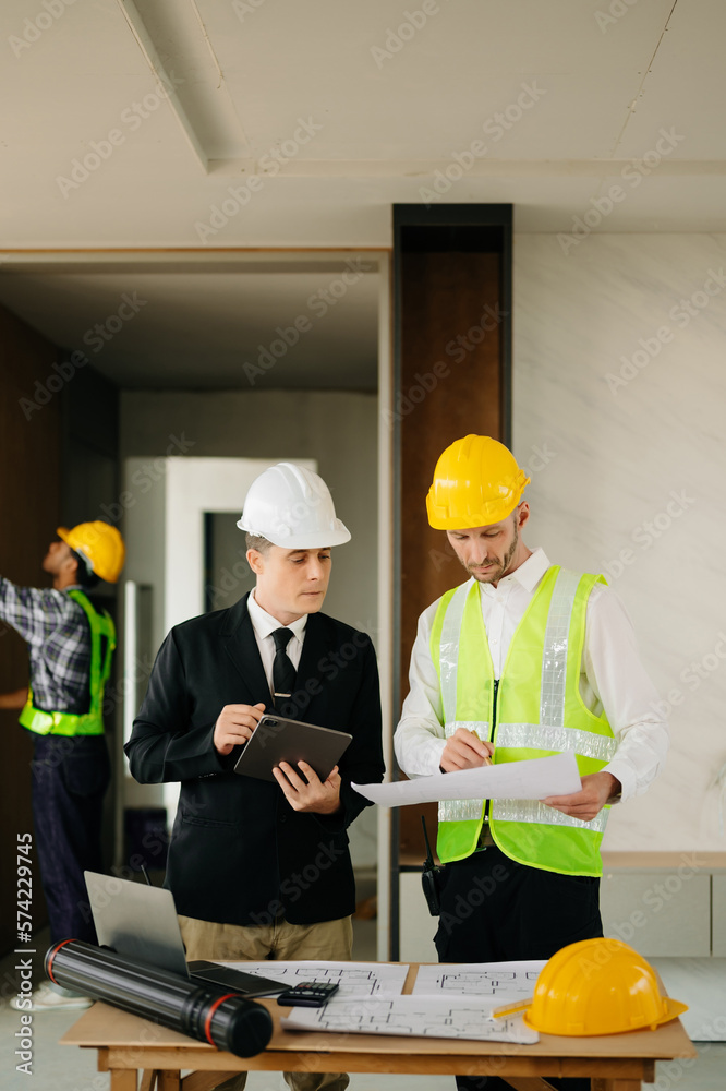 Contractor and architect looking at plan, tablet, laptop and talking about working on big project. B